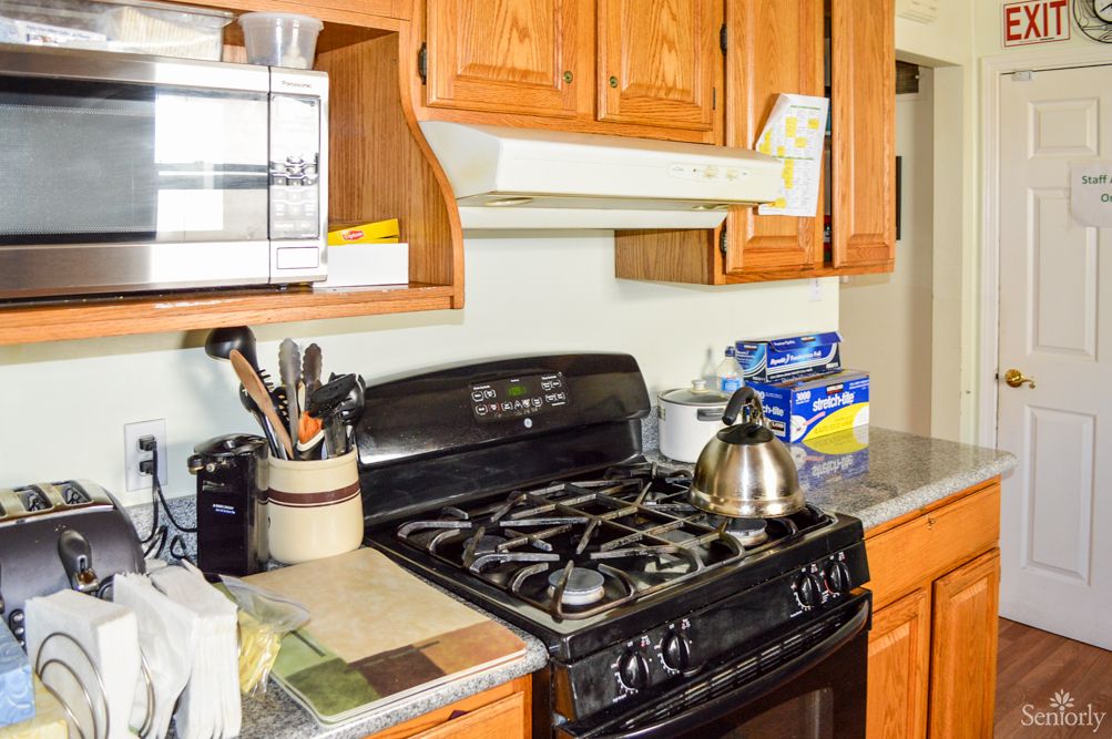 A kitchen featuring a stove with an oven, wooden cabinets, a microwave, and various kitchen utensils on the countertop.