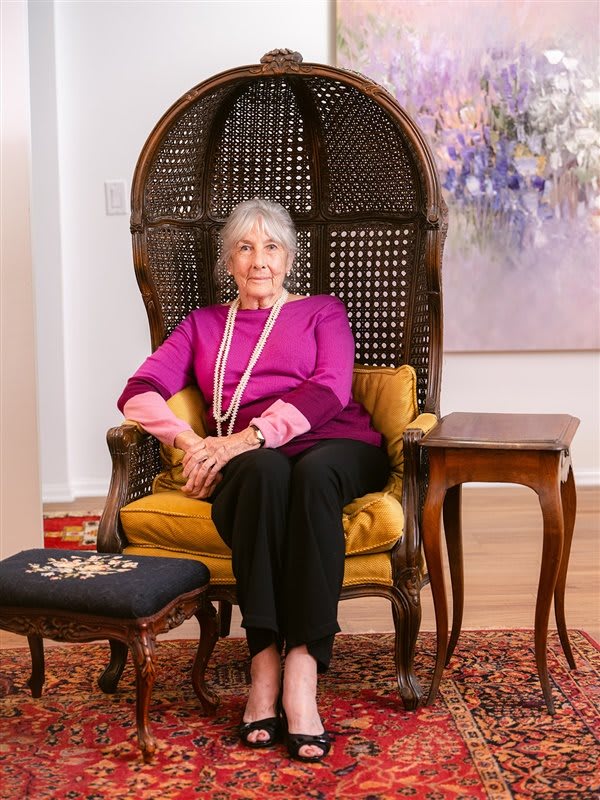An elderly woman sits comfortably on a chair in a well-decorated living room.