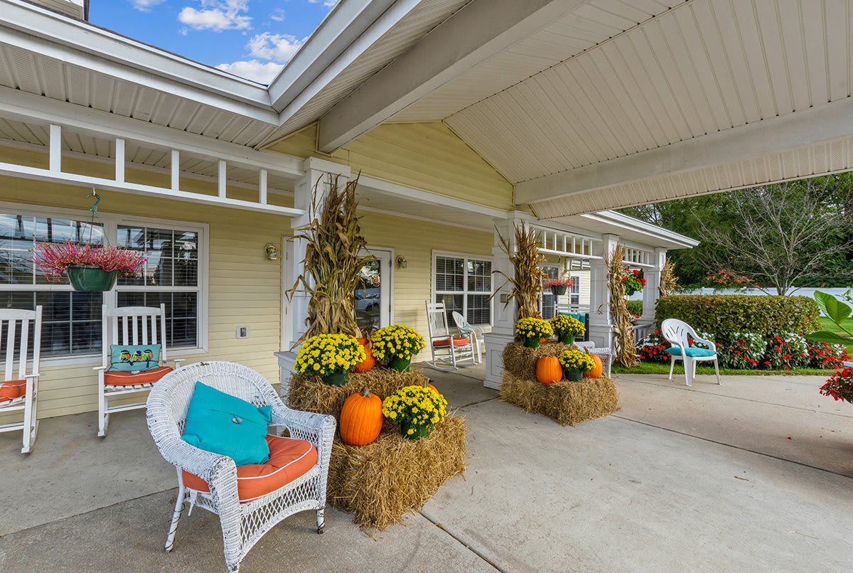 A cozy porch decorated with pumpkins, hay bales, and colorful flowers for autumn.