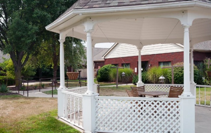 A white gazebo with lattice design in a garden setting, featuring outdoor furniture.