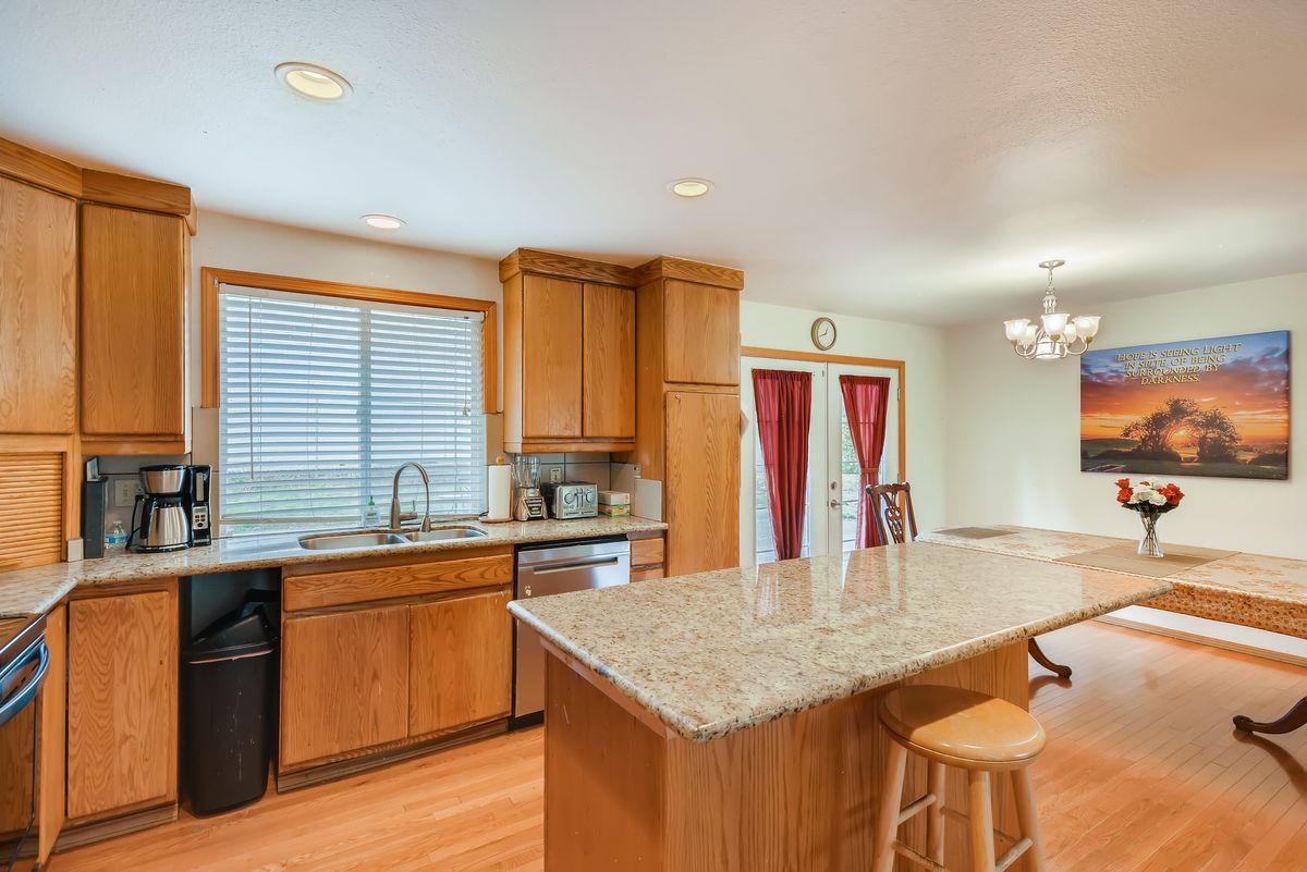 A modern kitchen with wood cabinets and a granite countertop island, showcasing open space and ample natural light.