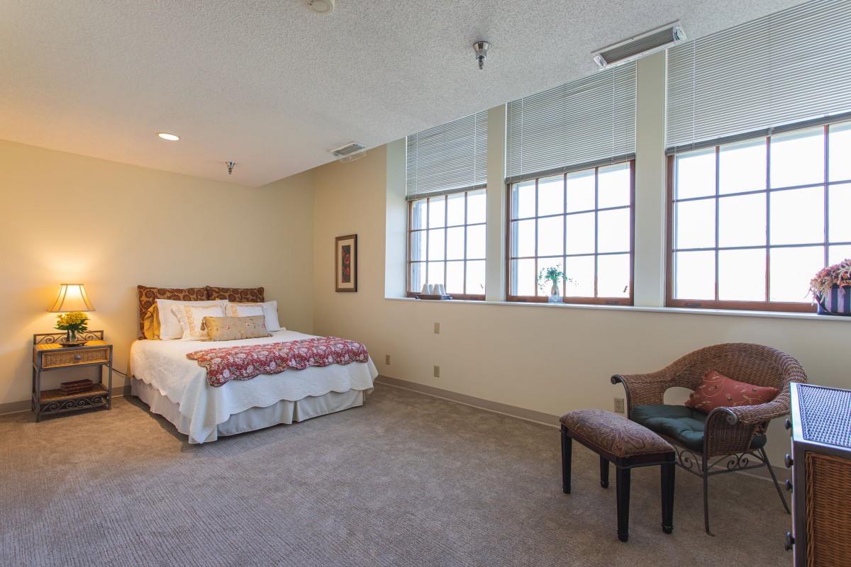 A minimalist bedroom with a large bed and ample natural light from multiple windows.
