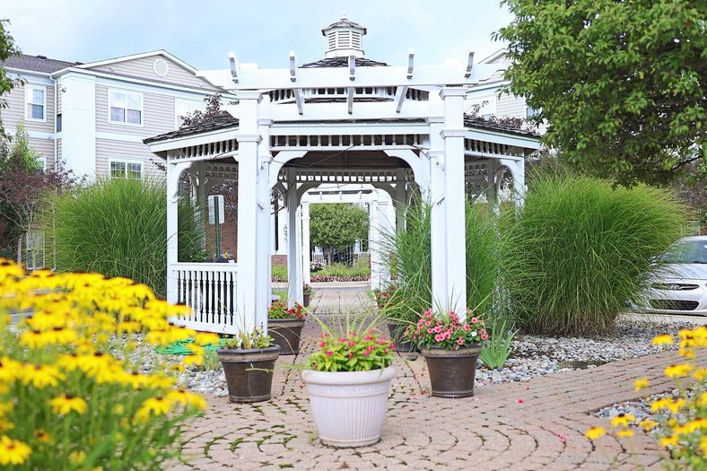 A picturesque outdoor garden featuring a white gazebo surrounded by lush greenery and colorful flowers.