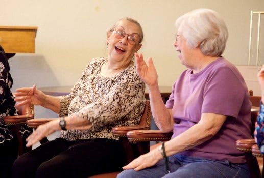 Two elderly women laughing and enjoying each other's company indoors.