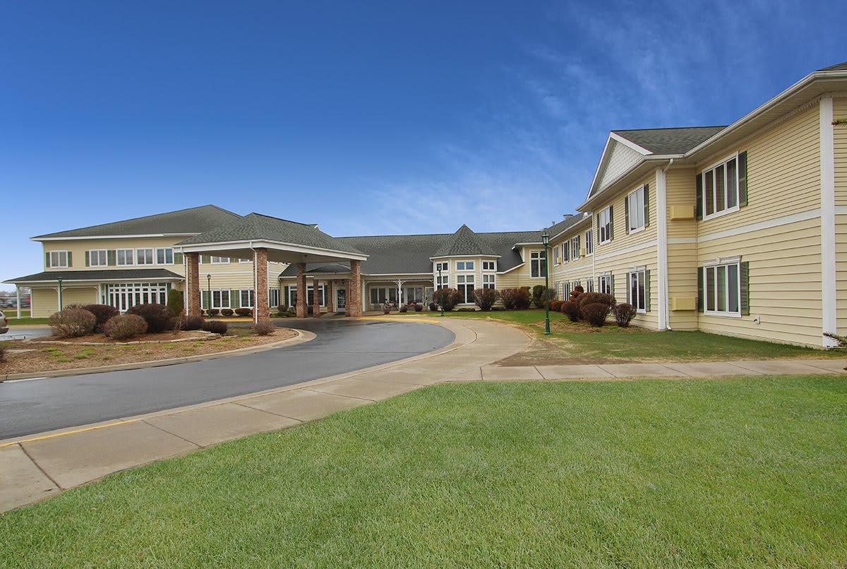 A large residential building with a well-maintained lawn and a circular driveway under a clear blue sky.