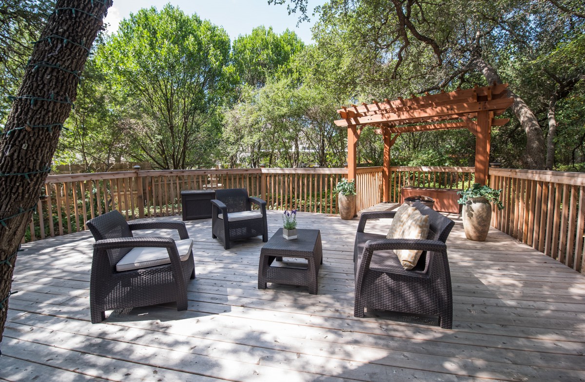 A peaceful outdoor deck with comfortable seating and a pergola surrounded by lush greenery.
