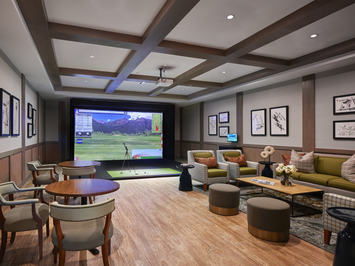 A modern recreation room featuring a golf simulator and comfortable seating arrangements.