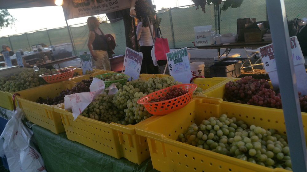 A variety of grapes displayed in yellow containers at an outdoor market.