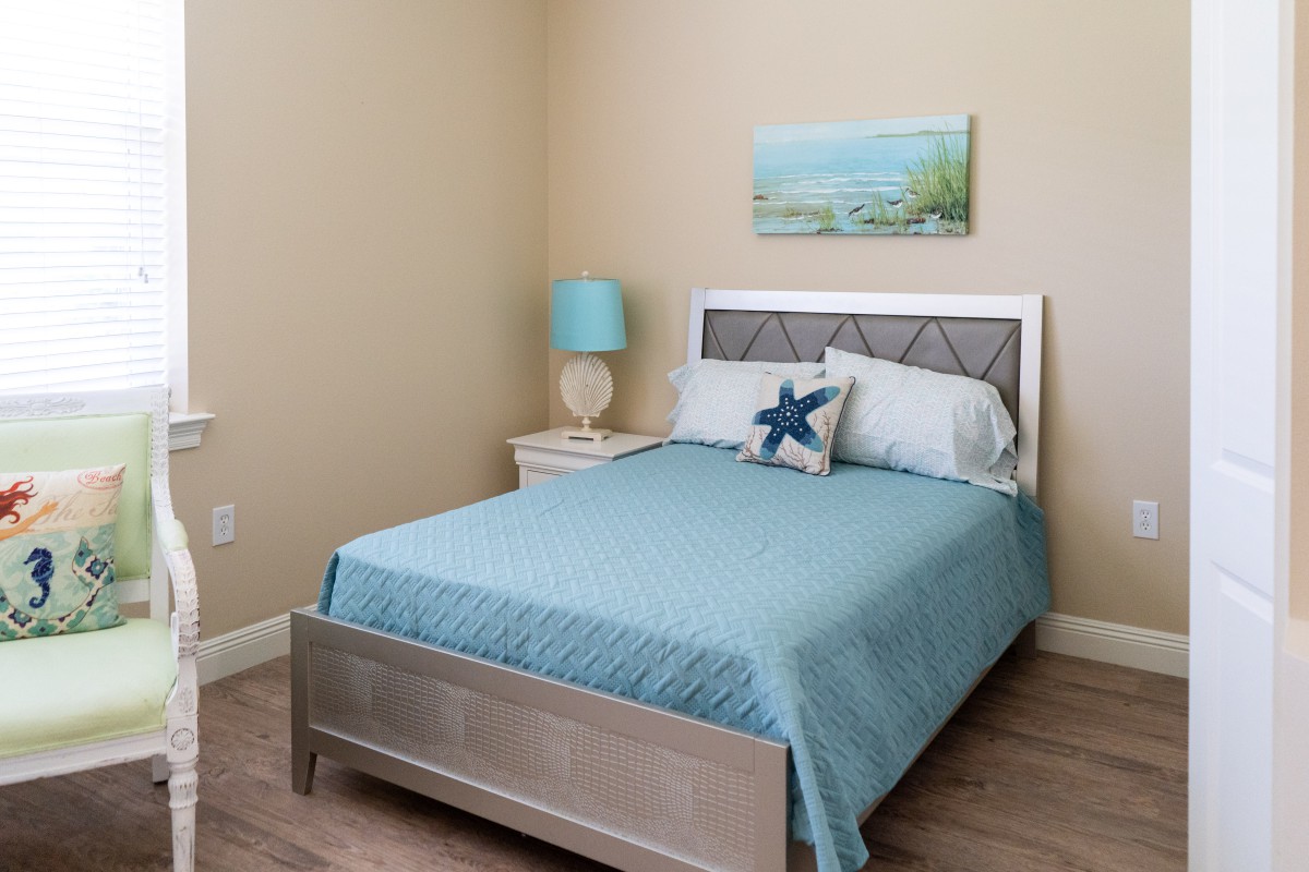 A cozy bedroom with a blue-themed decor, featuring a neatly made bed and a nightstand with a lamp.