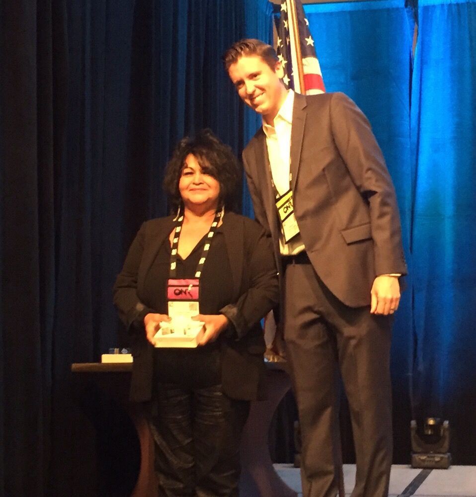 Two individuals posing for a photo on stage during an award ceremony.