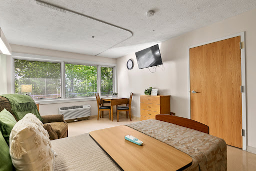 A cozy room featuring a bed, dining area, and large windows allowing natural light.