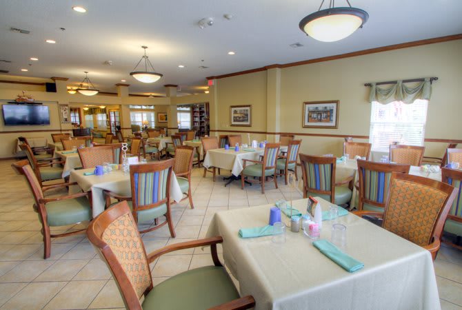 A spacious and elegantly decorated dining room with neatly arranged tables and chairs, featuring ambient lighting.