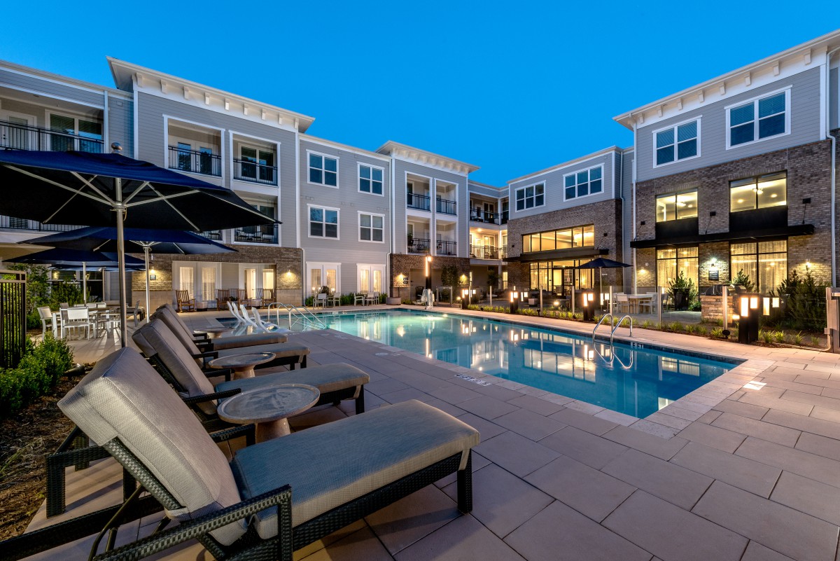 A beautifully lit swimming pool area in a modern luxury apartment complex during the evening.