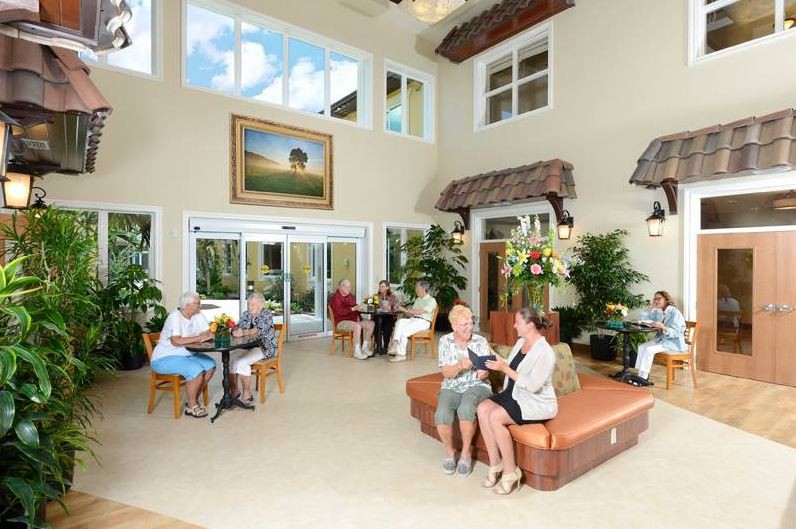 A bright and spacious lobby with people socializing in a comfortable seating area, surrounded by plants and artwork.