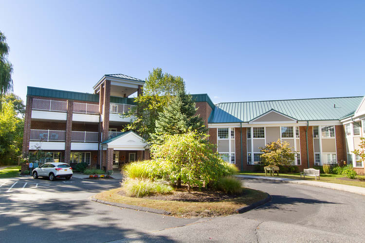 A modern hotel building surrounded by trees and landscaping under a clear blue sky.