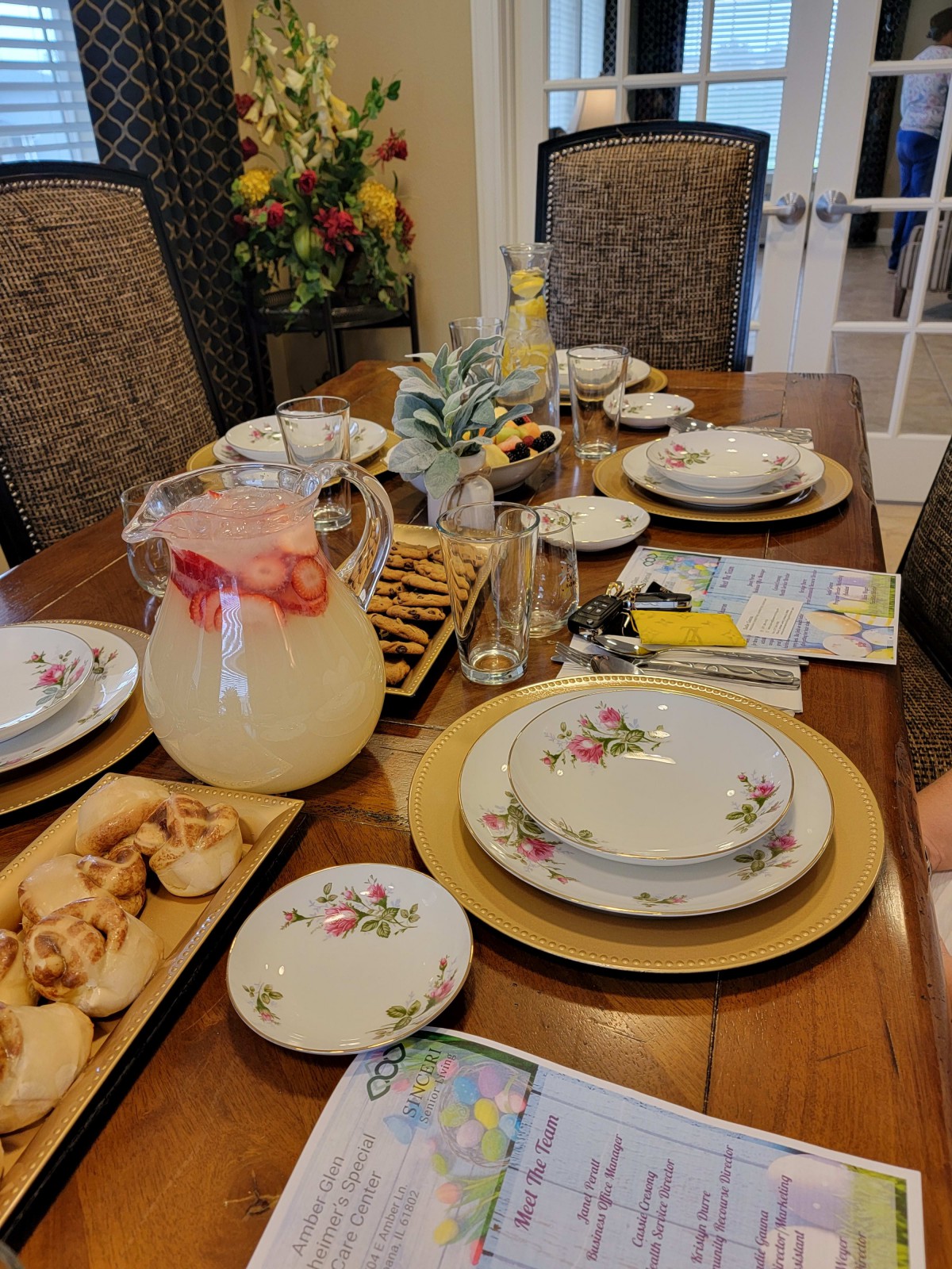 A beautifully set dining table prepared for a meal, featuring elegant plates, glassware, a pitcher of beverage, and decorative flowers.