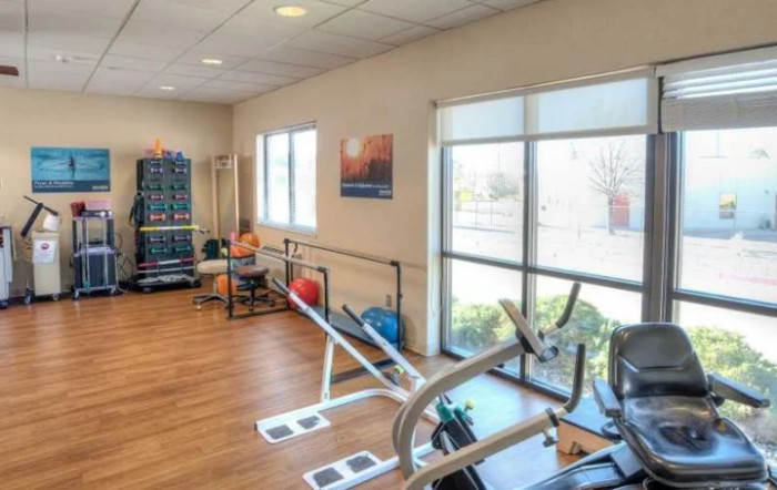 A bright and spacious gym with exercise equipment, weights, and large windows.