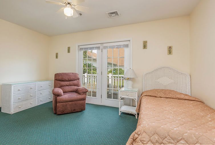 A cozy bedroom with a bed, armchair, and large patio doors leading outside.