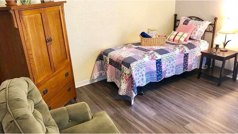 A cozy bedroom with a quilt-covered bed, wooden wardrobe, and armchair.
