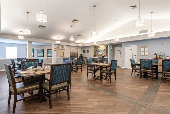 A well-lit dining area with neatly arranged tables and chairs, featuring elegant lighting and a wooden floor.