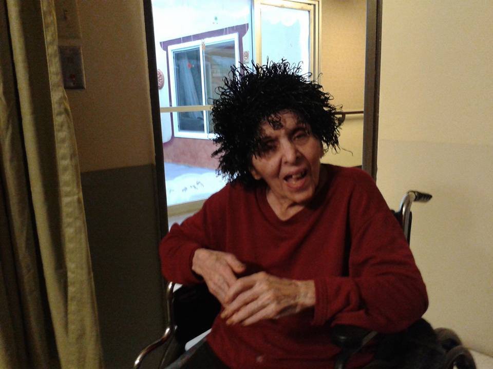 A person in a wheelchair wearing a curly wig and smiling indoors.