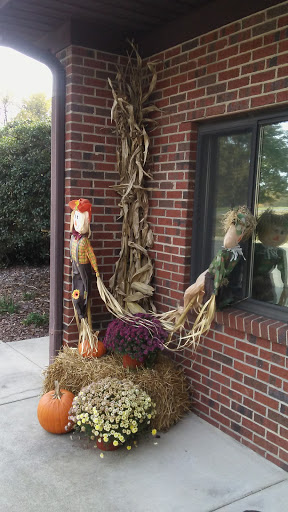 A charming autumn display featuring corn husk dolls, pumpkins, and vibrant flowers on a welcoming porch.