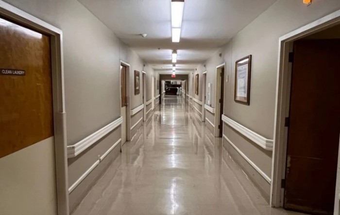 A long, well-lit hospital hallway with clean floors and closed doors on either side.