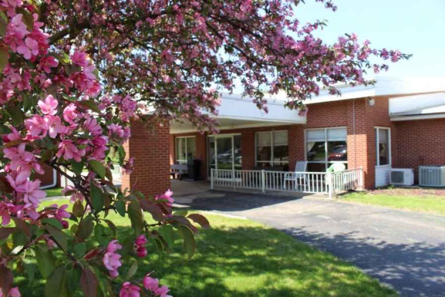 A brick house with a charming porch surrounded by blossoming flowers on a sunny day.