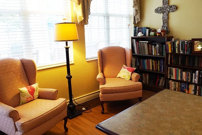 A cozy living room with two armchairs, a standing lamp, and a bookshelf by a window.