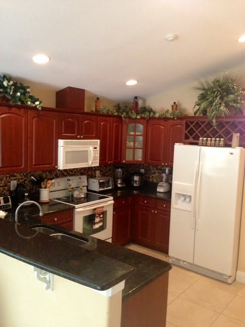 A modern kitchen with wooden cabinets and various appliances, including a refrigerator, microwave, and oven.