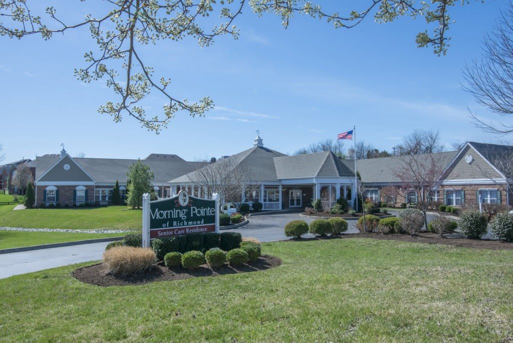 A scenic view of a building with a prominent sign on a sunny day, surrounded by well-maintained lawns and trees.