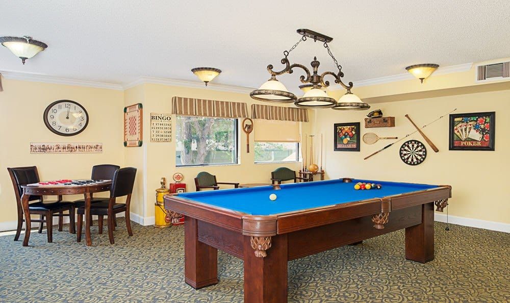 A cozy game room featuring a pool table with blue felt, surrounded by comfortable seating and classic decor.