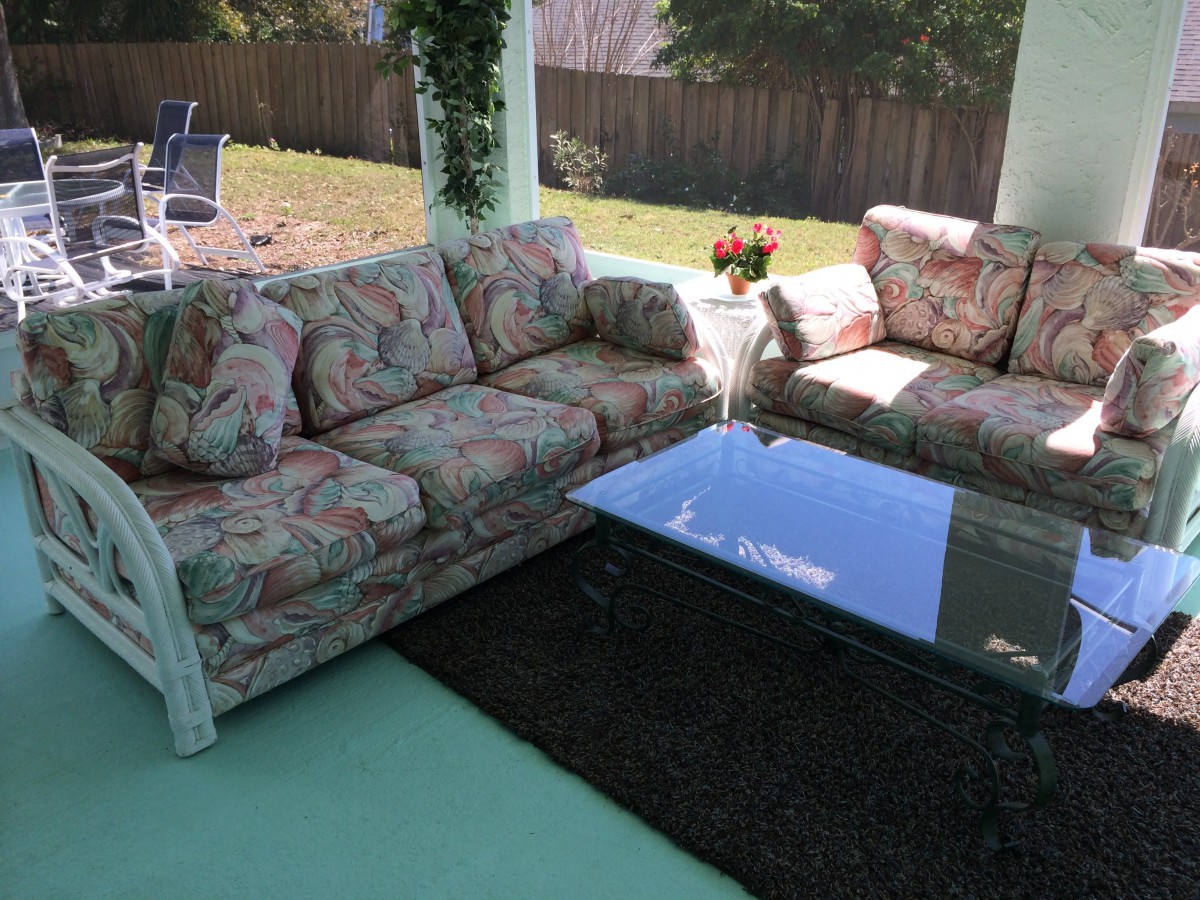 A cozy outdoor patio area featuring a floral-patterned sectional sofa and a glass-top coffee table.