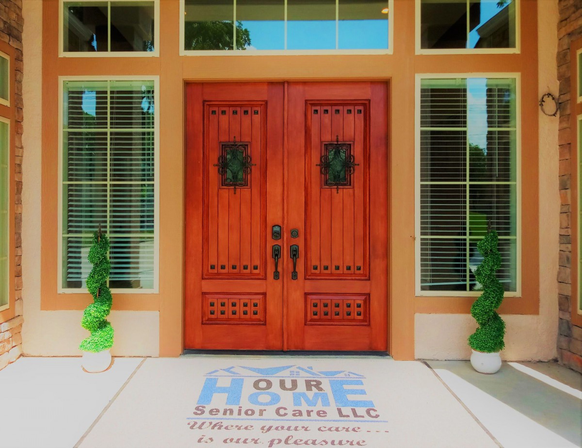 A welcoming double wooden front door flanked by large windows and decorative plants.
