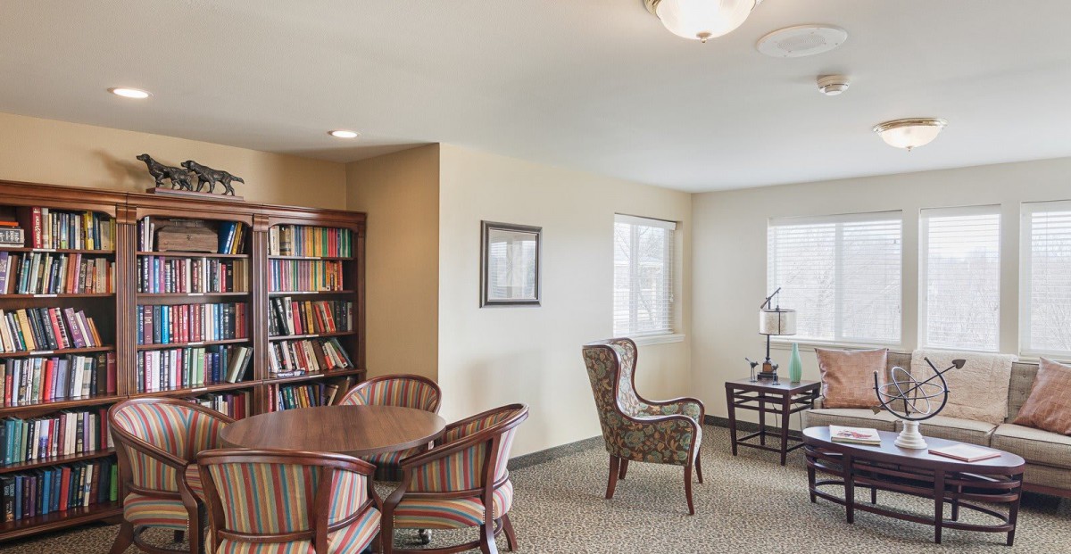 A cozy living room with a bookshelf, table, and comfortable chairs.