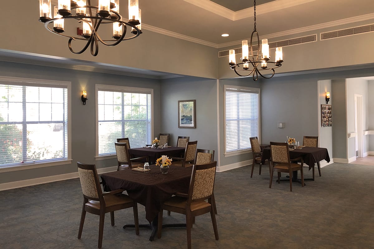 A well-lit dining room with elegant chandeliers and neatly arranged tables and chairs.