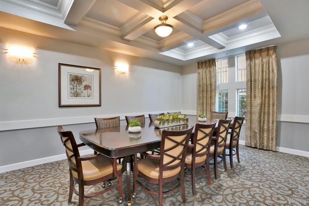 A well-lit dining room with a large table, surrounded by chairs, featuring elegant lighting and decor.