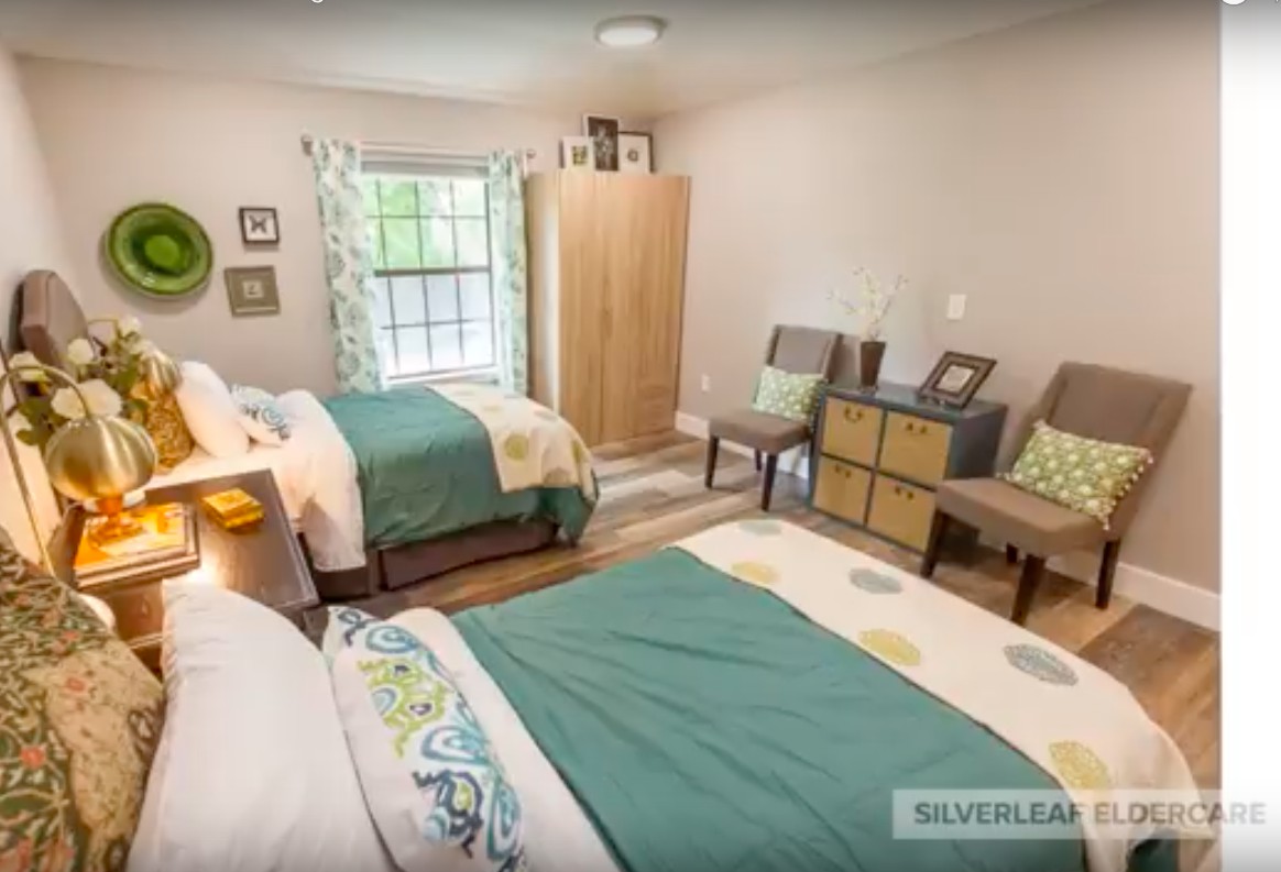 A cozy bedroom with two beds, a wardrobe, and chairs by the window.