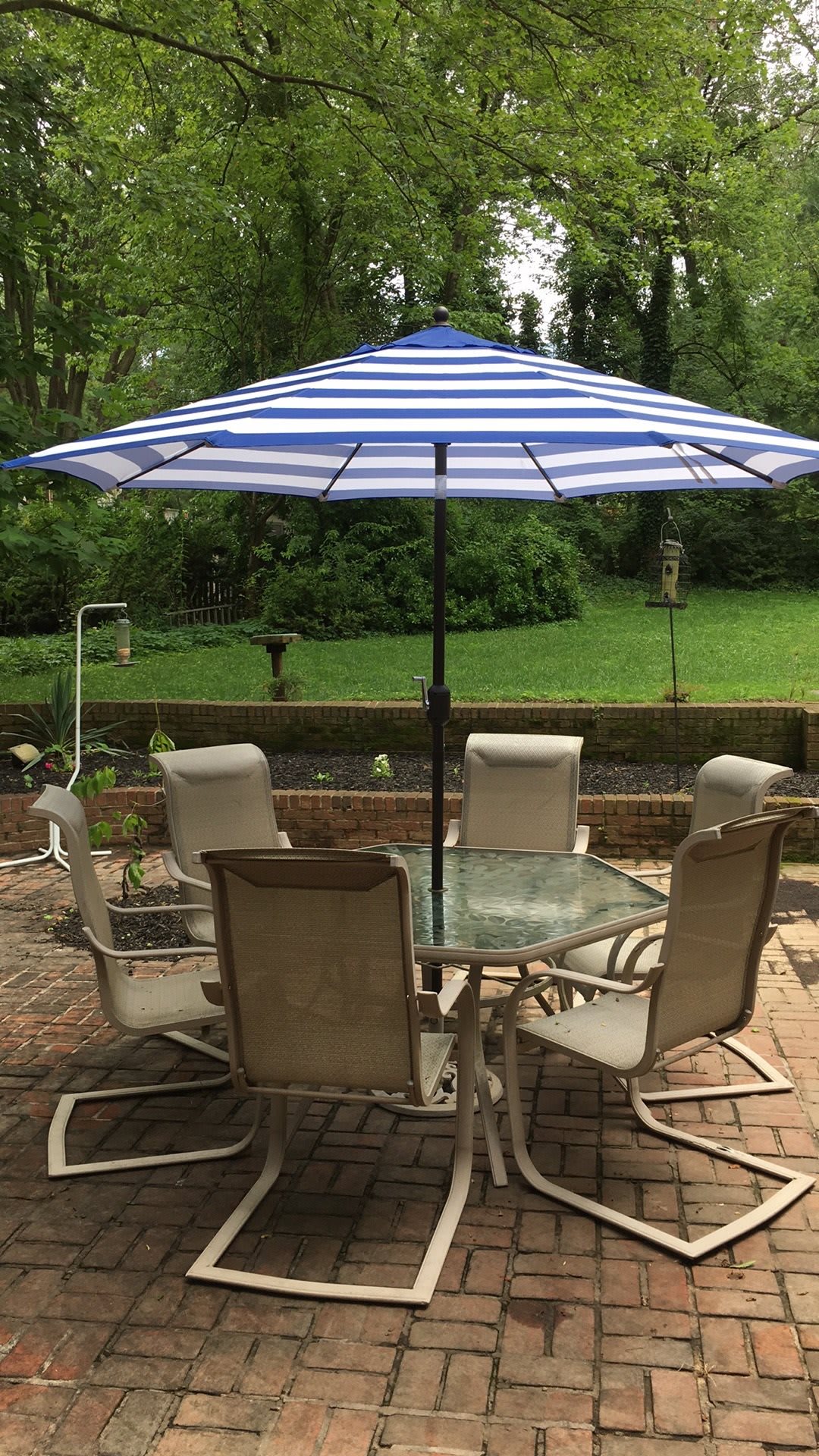 A cozy outdoor patio set with a blue and white striped umbrella, surrounded by greenery.