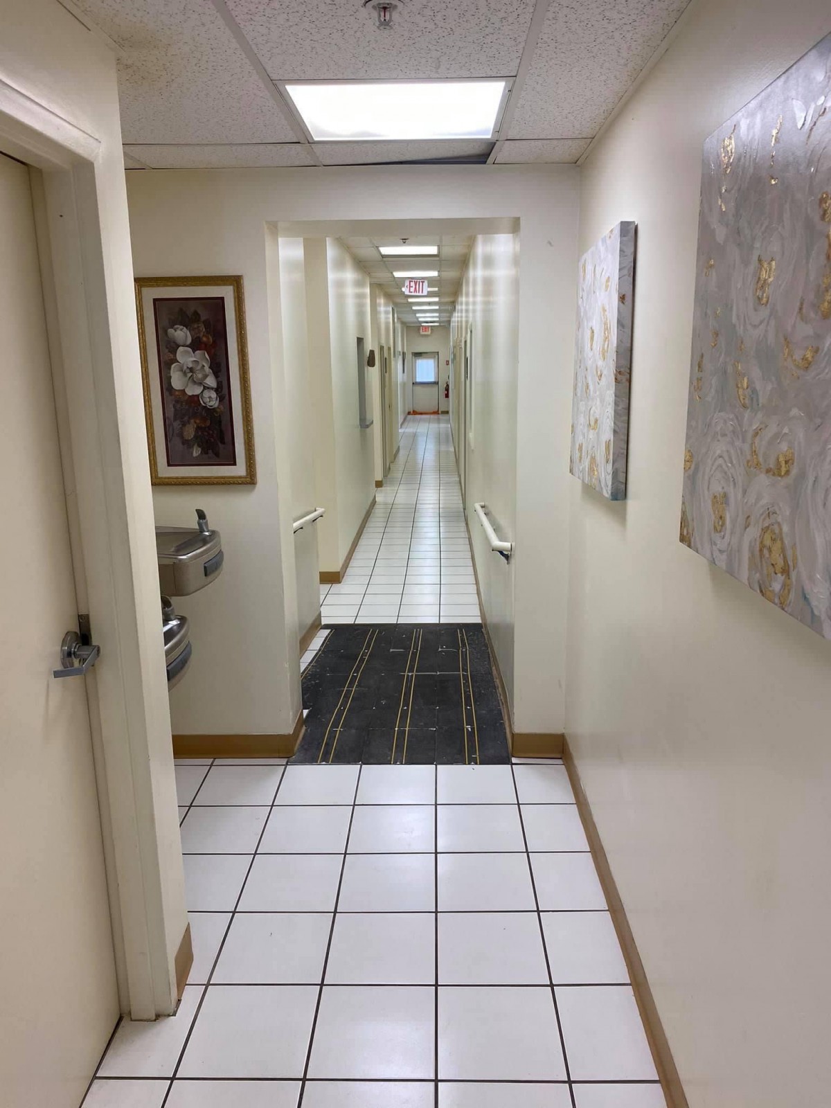 A long indoor hallway with tiled flooring, artwork on the walls, and a water fountain.