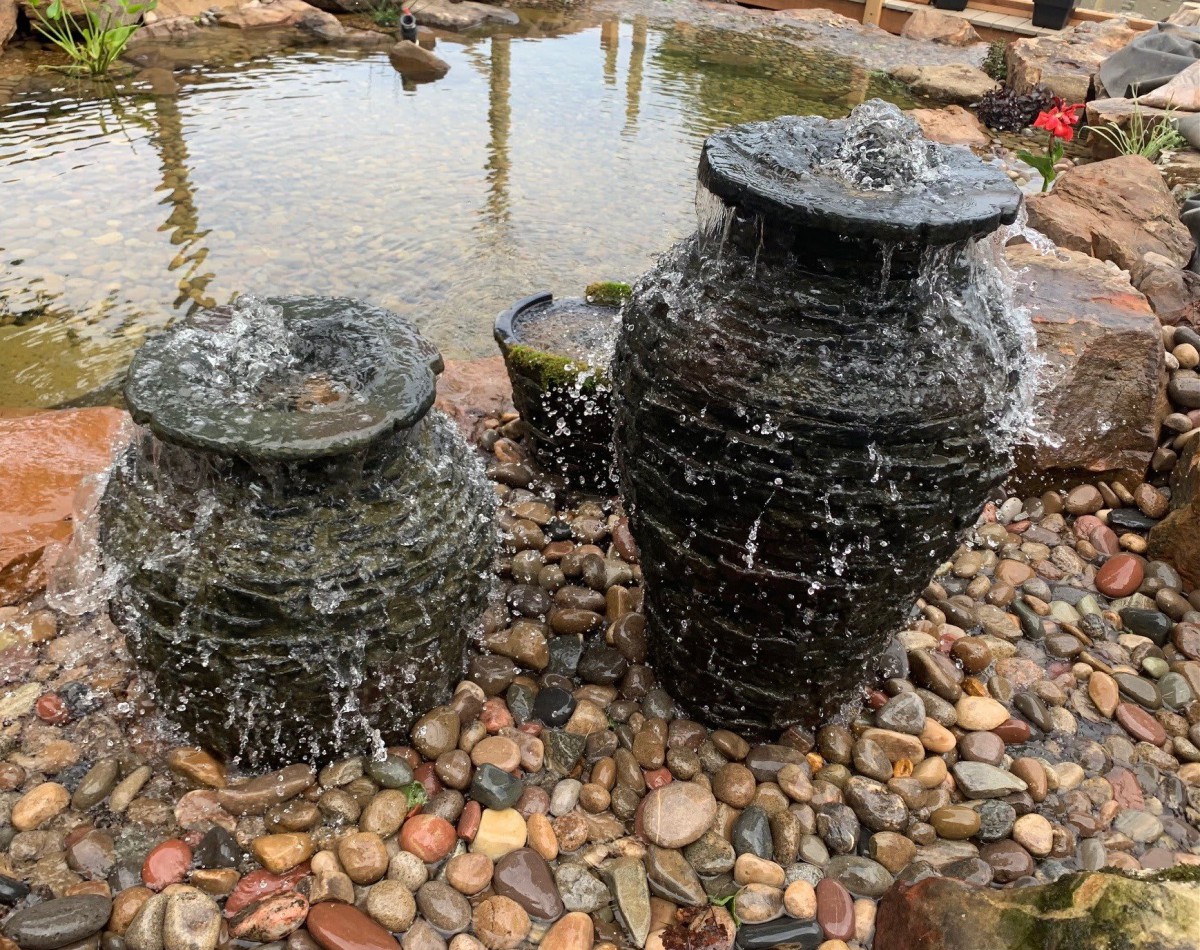 A pair of stone pot fountains with water gently cascading over them in a garden setting.
