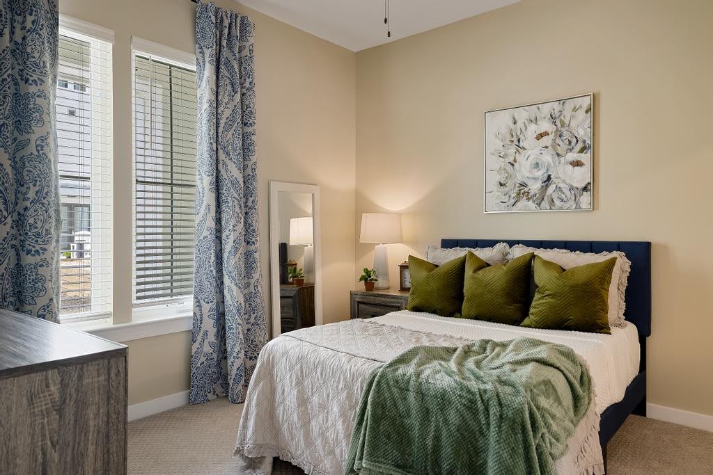 A modern bedroom with stylish decor, featuring a neatly made bed with green accents and elegant curtains.