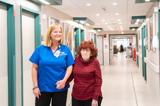 A nurse assists an elderly woman as they walk through the hospital corridor.