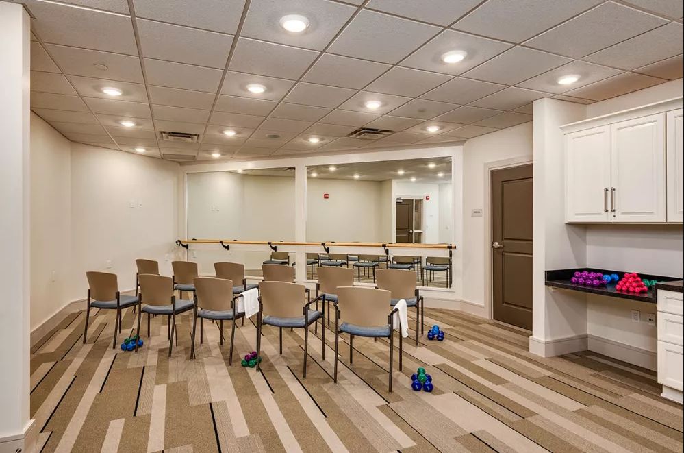 An exercise room with chairs, mirrors, and dumbbells on a wooden floor.