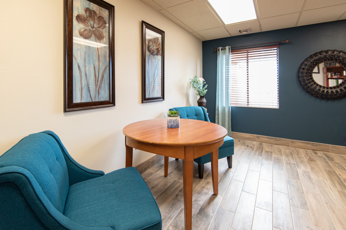 A small meeting room with two blue chairs, a wooden table, and artwork on the walls.