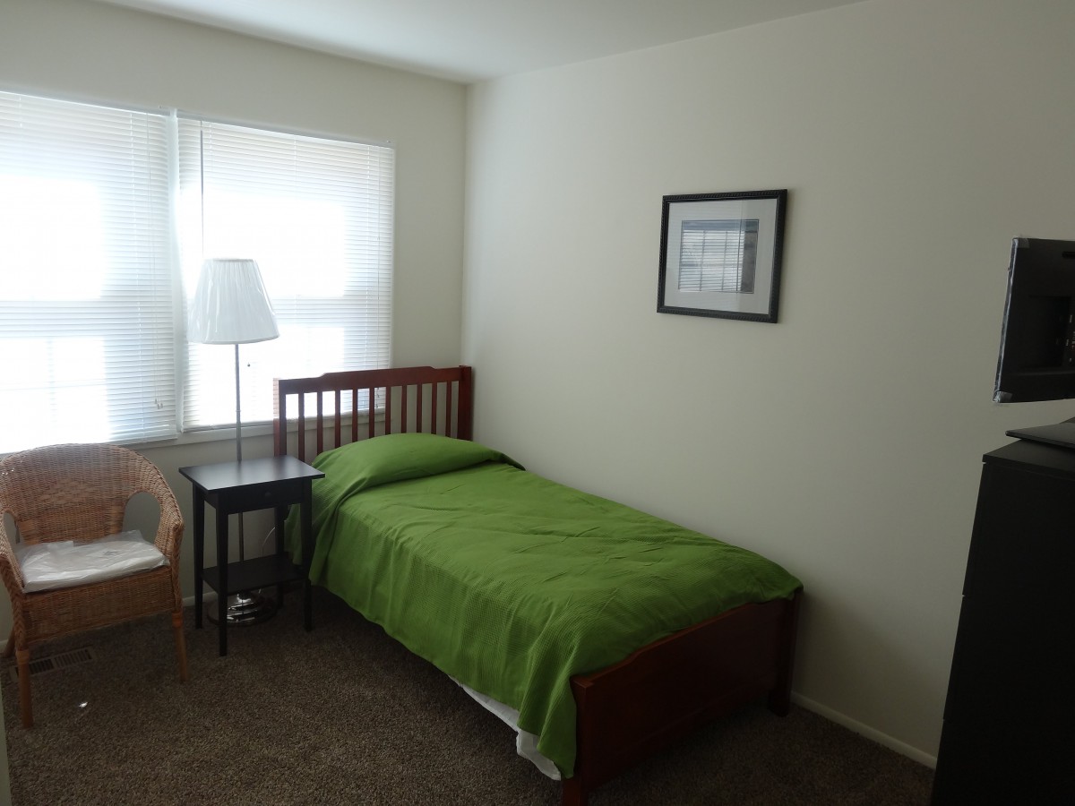 A simple bedroom with a single bed, green bedding, and minimal decor.