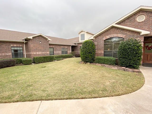 A suburban brick house with a neatly maintained lawn and shrubs under a cloudy sky.