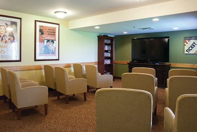 A small meeting room with rows of comfortable chairs facing a large television.