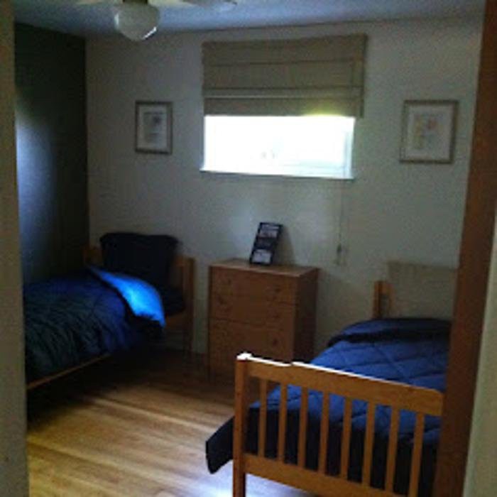 A small bedroom featuring two twin beds with dark bedding and a chest of drawers beneath a window.
