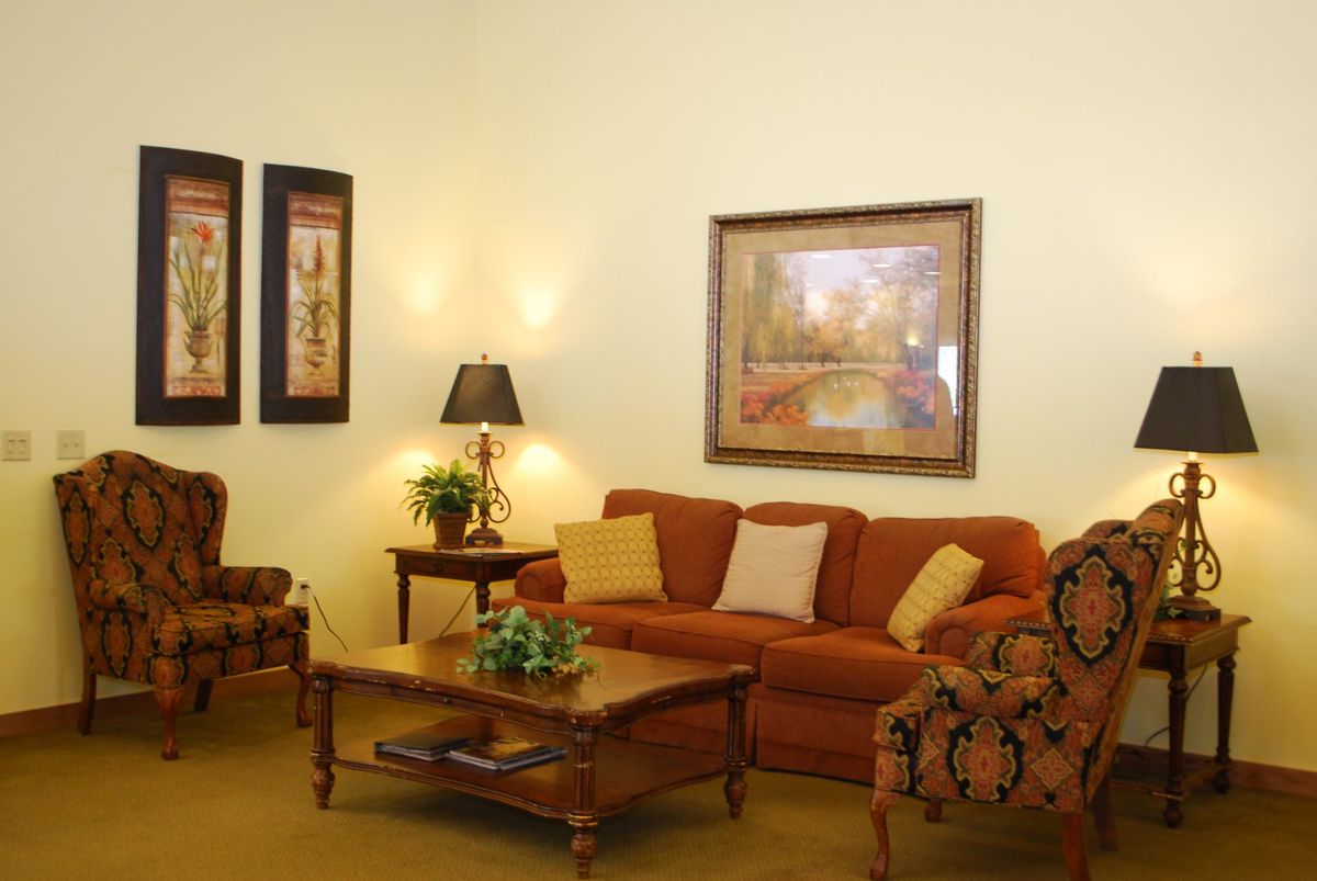 A cozy living room featuring a sofa with decorative pillows, armchairs, a wooden coffee table, and framed artwork on the walls.